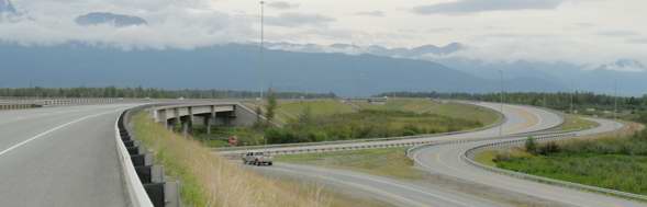 South end of George Parks Highway, at junction with Glenn Highway, with through lanes from the Parks to the westbound Glenn on the bridge to the left, the Glenn passing under that bridge, the ramp from the Parks to the eastbound Glenn in the center, and a frontage road to the right