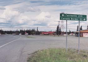 Junction of Tok Cutoff with the Alaska Highway, in ther background; sign in foreground: 208 miles left to Fairbanks, 90 miles right to Canada border