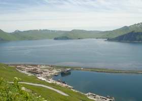 View of east end of harbor and its breakwater, with snippet of Ulakta Drive to lower right, and mountains in background